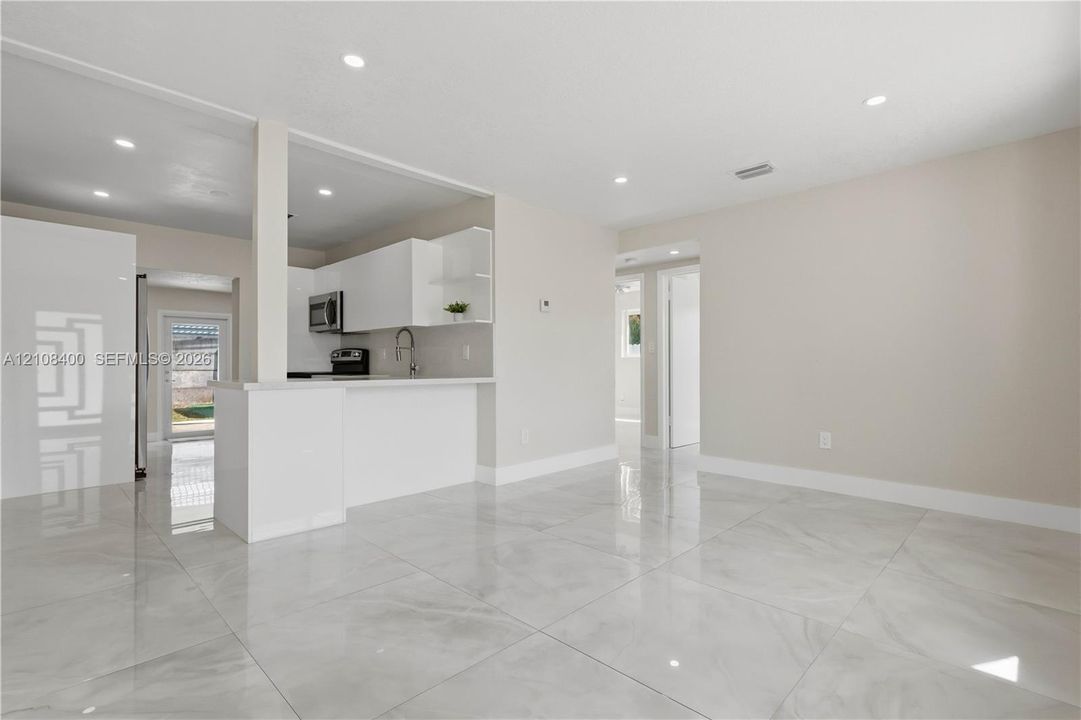 Open-concept interior featuring large-format tile flooring, white cabinetry, integrated peninsula, and recessed lighting