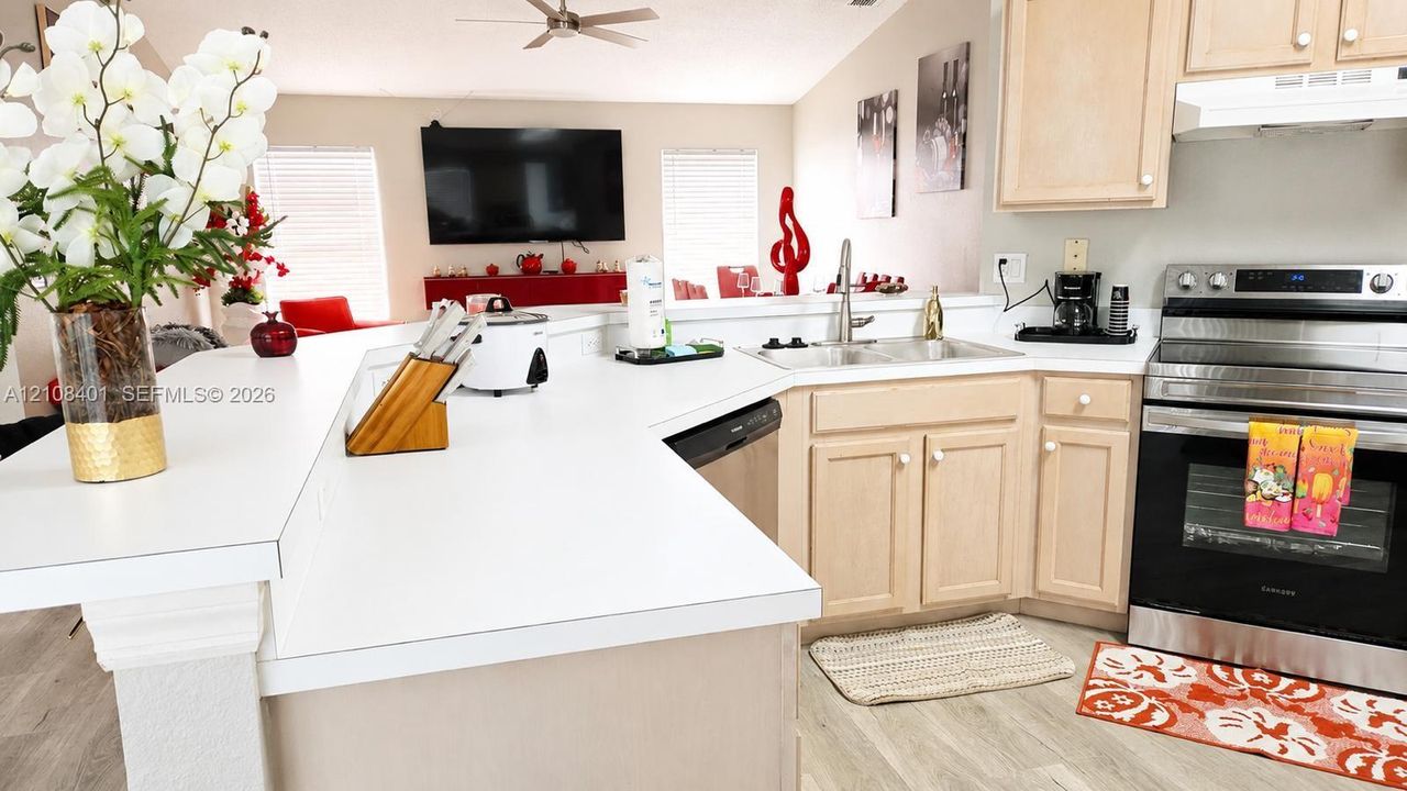 Kitchen featuring a tiered peninsula, light wood-finish cabinetry, solid-surface countertops, a stainless steel range, and wood-finish flooring