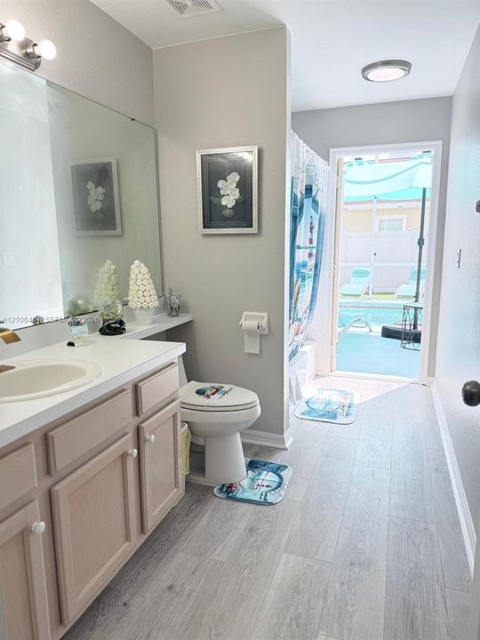 Bathroom featuring wood-finish flooring, vanity with countertop basin, full-width wall mirror, and integrated tub and shower combination with direct exterior access