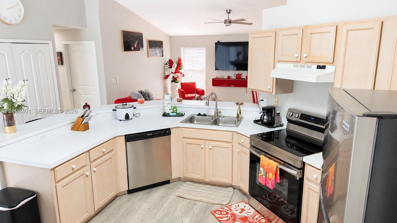 Kitchen featuring light-tone cabinetry, stainless steel appliances, solid-surface countertops, dual-basin stainless steel sink, and wood-finish flooring