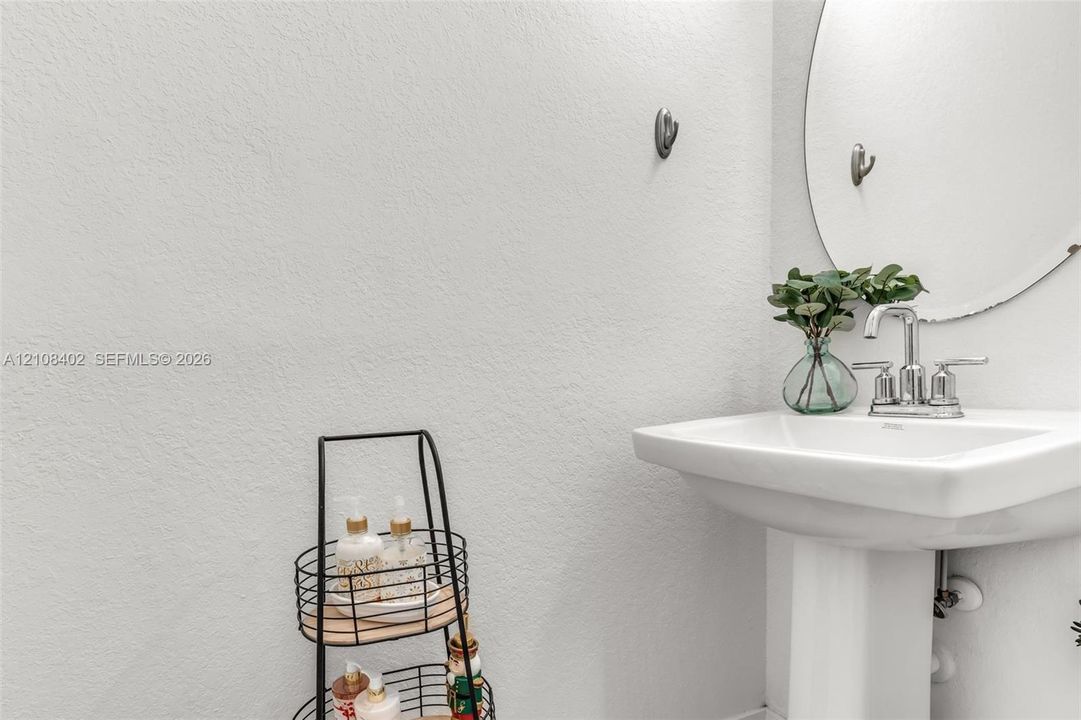 Pedestal sink featuring a polished chrome faucet and a circular wall-mounted mirror