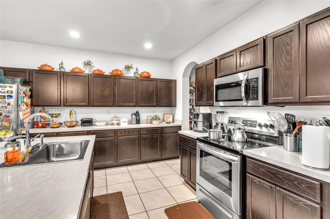 Kitchen featuring dark-stained cabinetry, stainless steel appliances, quartz countertops, a double-basin stainless steel sink, and tile flooring