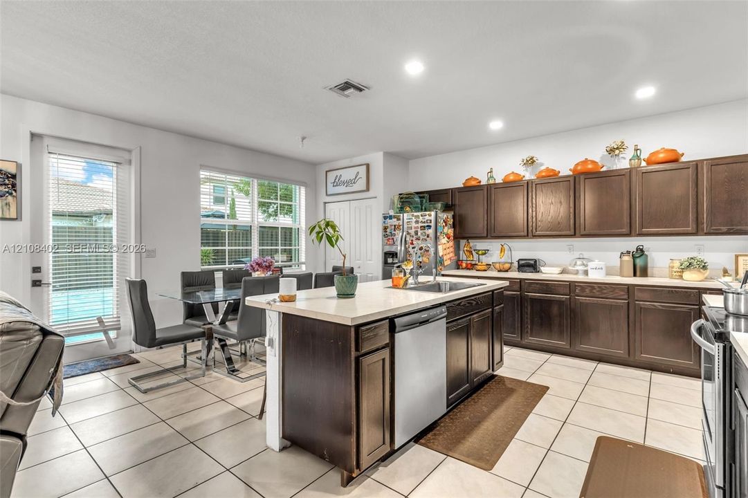 Kitchen featuring stained wood cabinetry, stone-finish countertops, a center island with an integrated stainless steel dishwasher, tile flooring, and large windows