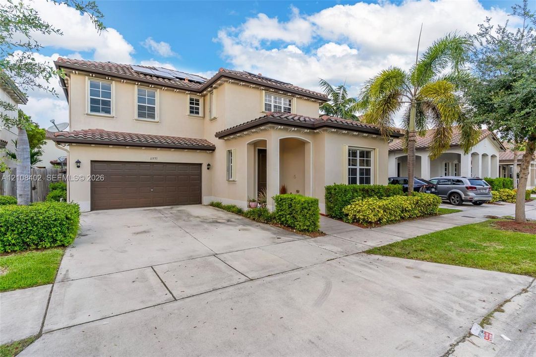 Two-story stucco exterior featuring a tiled roof, integrated solar panels, a multi-car garage, and manicured landscaping