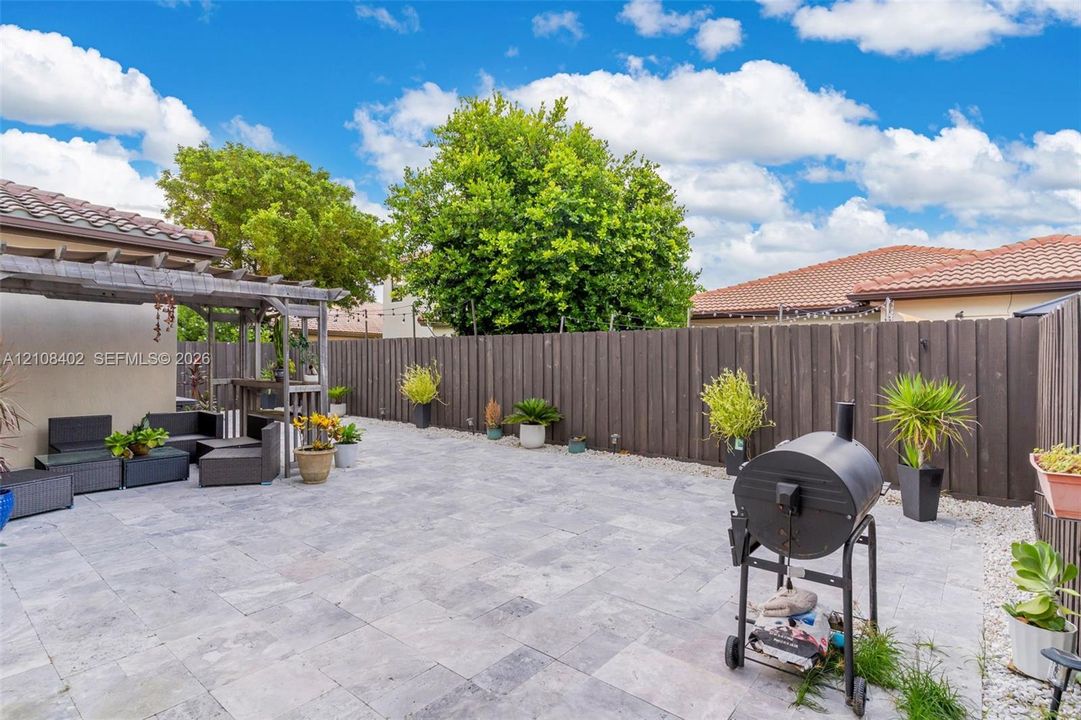 Outdoor living area featuring a neutral-toned stone paver patio, a wooden pergola, and a full-height privacy fence