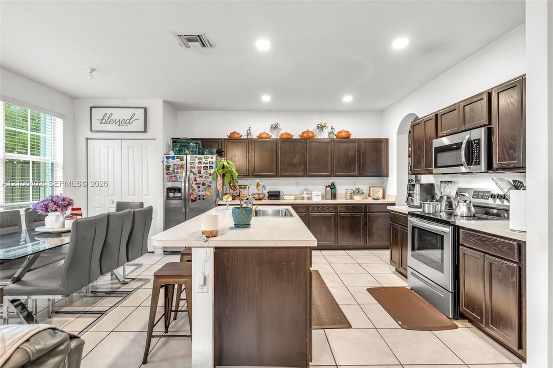 Kitchen featuring dark-finish wood cabinetry, a central island with a solid surface countertop, tile flooring, and stainless steel appliances