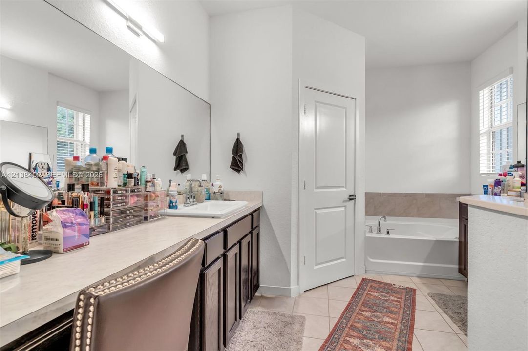 Bathroom featuring an expansive vanity with dark-finish cabinetry, a large wall-to-wall mirror, a rectangular drop-in sink, and a separate soaking tub with tiled surround