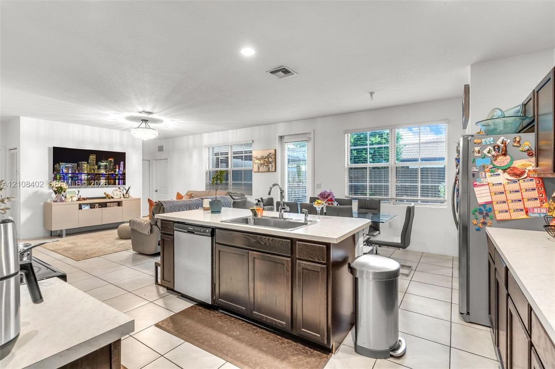 Kitchen featuring a central island with a stainless steel undermount sink, dark wood-finish cabinetry, solid-surface countertops, tile flooring, and stainless steel appliances