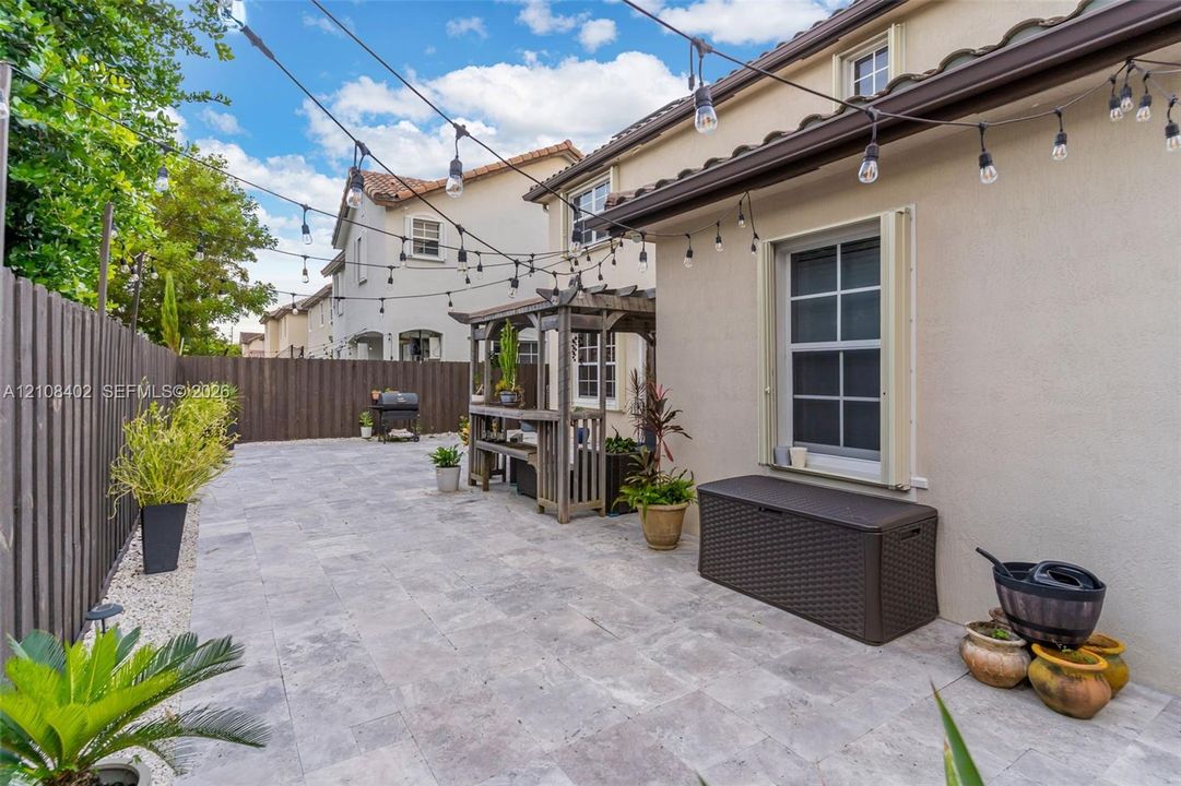 Paved patio featuring stone tile surfacing, wood-slat perimeter fencing, a built-in wooden pergola, and overhead string lighting
