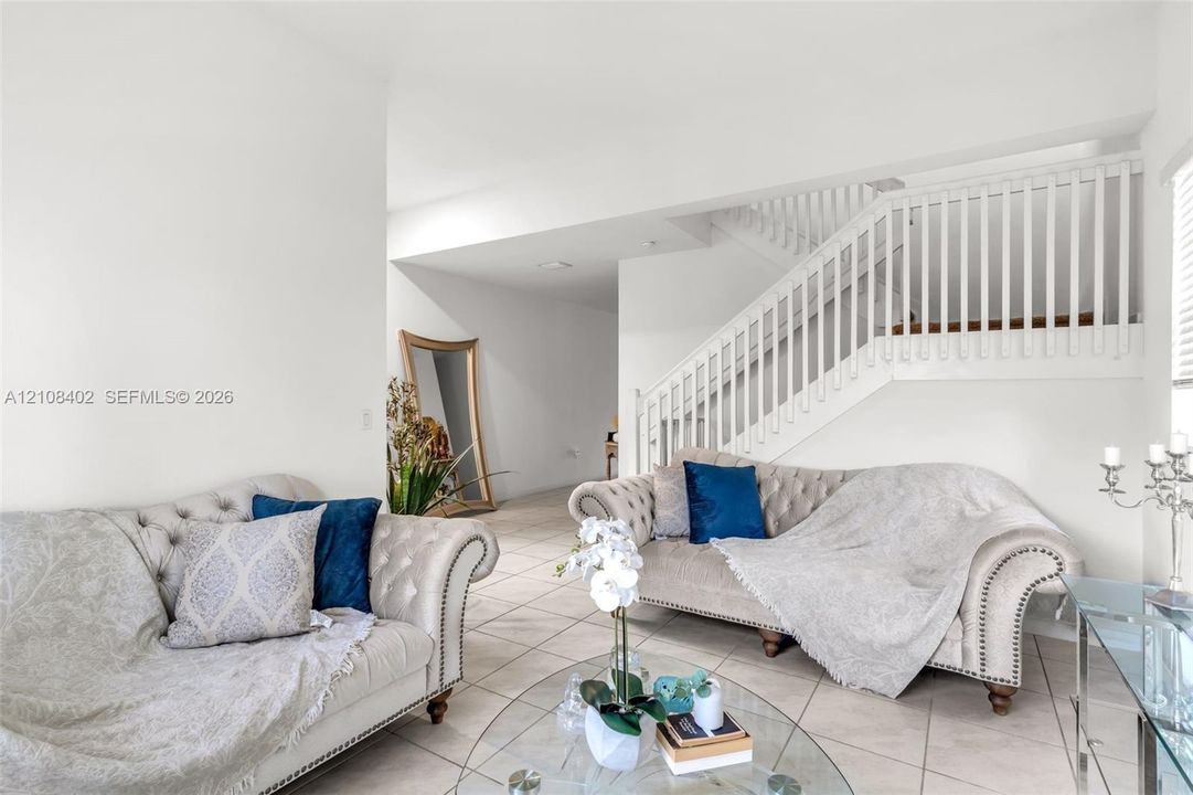 Open-concept interior featuring large-format ceramic tile flooring and a staircase with white vertical balusters