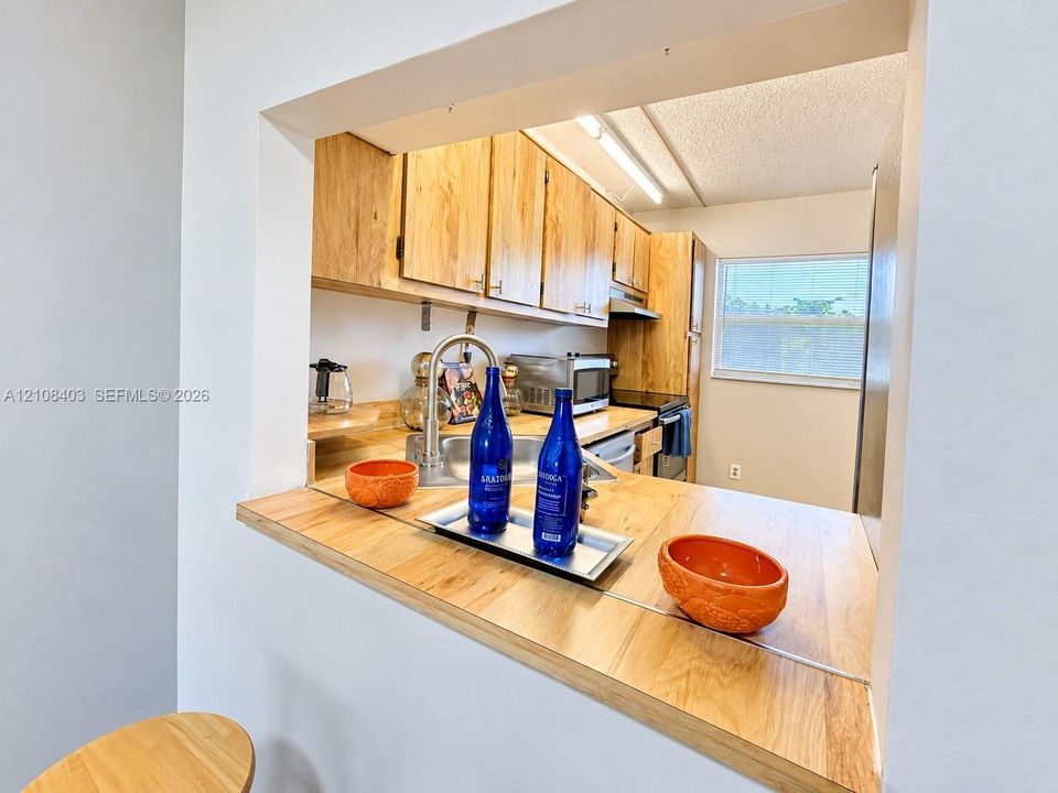 Kitchen pass-through window featuring a wood-finish countertop, stainless steel sink, gooseneck faucet, and light wood cabinetry