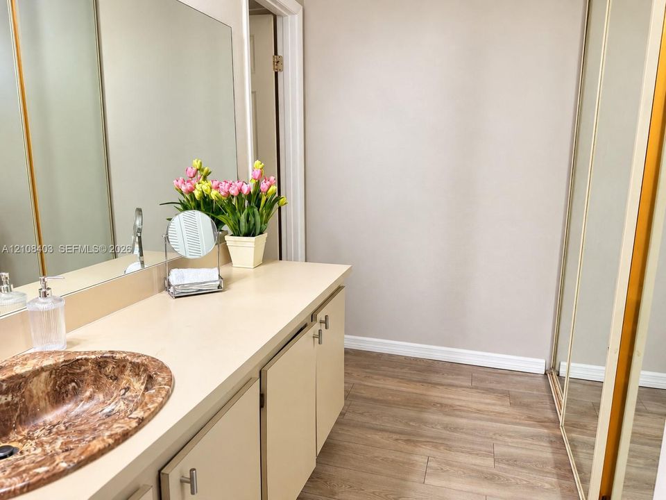 Master Bathroom vanity featuring a solid surface countertop, an oval inset stone-finish sink, extensive wall-spanning mirror, and wood-finish flooring