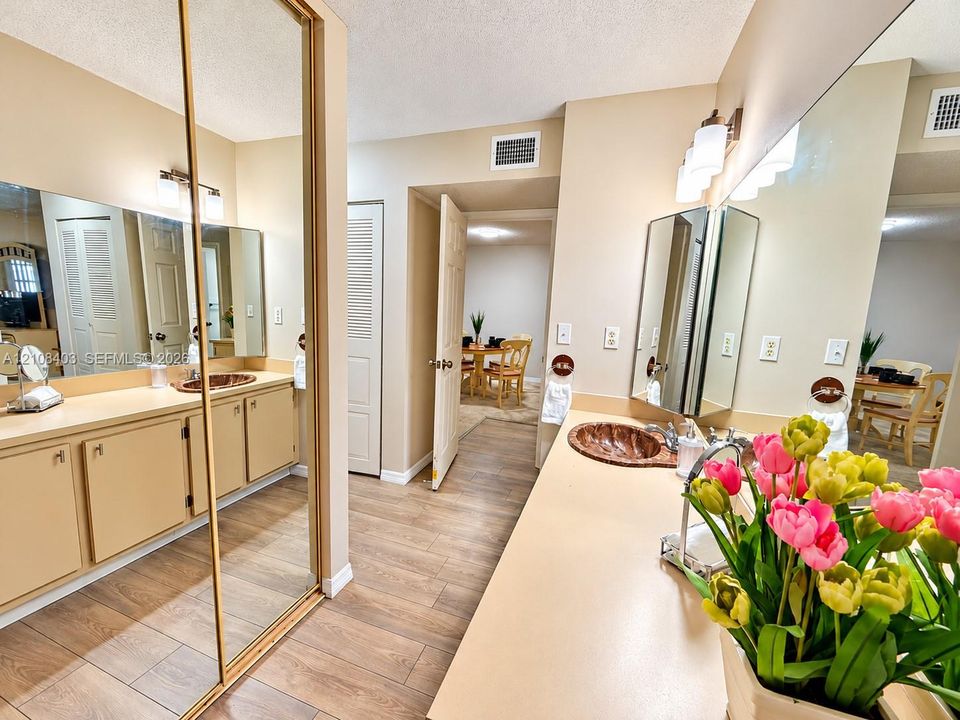 Located in the Master bathroom-  vanity area with custom-fitted mirror panels, solid surface countertops, textured copper-finish vessel sinks, and wood-finish flooring