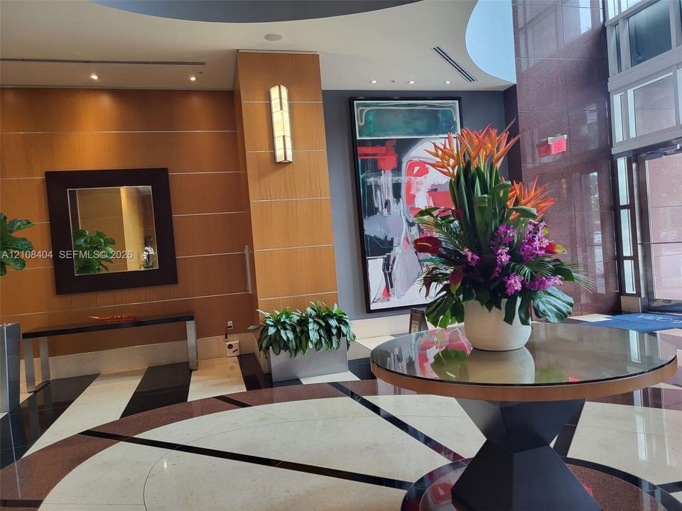 Entrance lobby featuring polished stone flooring with geometric patterns, wood-paneled walls, recessed ceiling lighting, and wall-mounted sconces