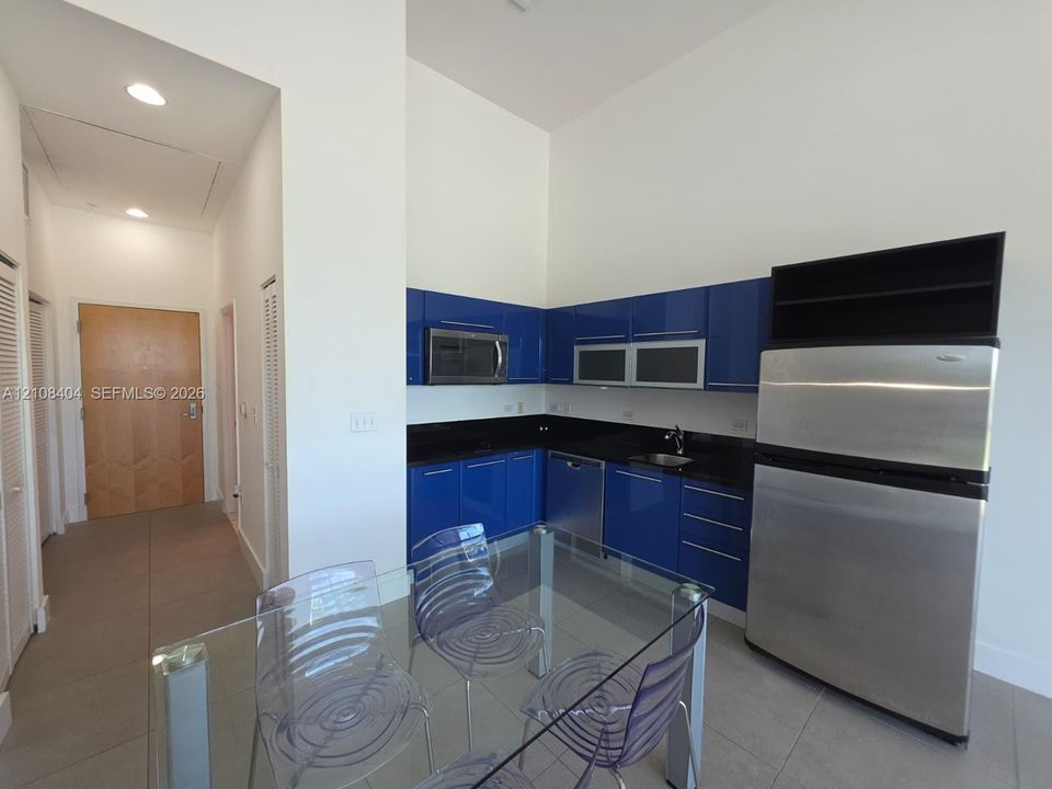 Kitchen featuring high-gloss blue cabinetry, dark stone countertops, stainless steel appliances, recessed ceiling lighting, and large-format tile flooring