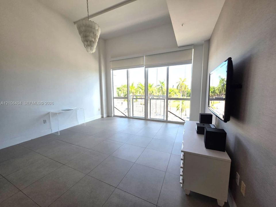 Living area featuring high ceilings, large-format tile flooring, a tiered chandelier, full-height windows with integrated shades, and a textured accent wall