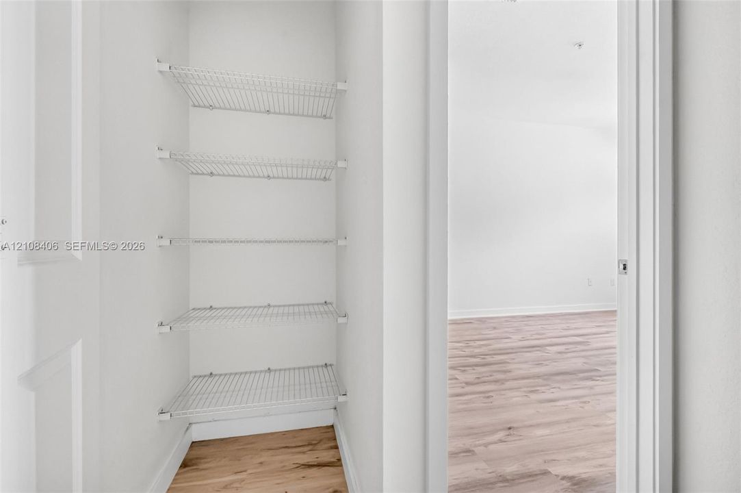 Storage closet featuring five tiers of white wire shelving and wood-finish flooring