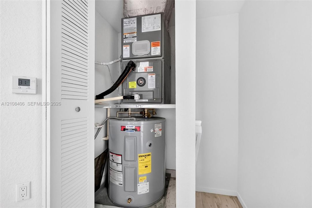Utility closet featuring a stacked forced-air heating and cooling unit with an integrated water heater and louvered access door