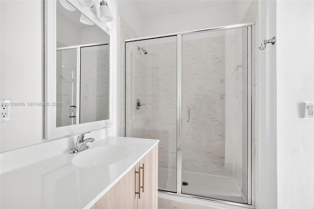 Bathroom featuring a light wood-finish vanity with a white countertop, walk-in shower with a glass enclosure, and wall-mounted mirror with integrated light fixtures
