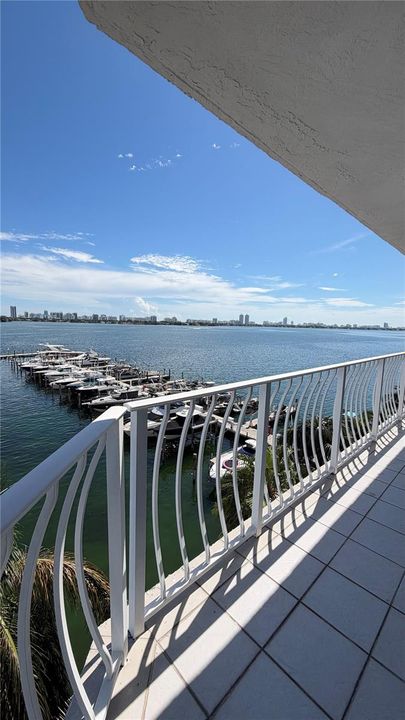 Covered balcony featuring white tile flooring and a decorative white metal railing, overlooking a marina and open water