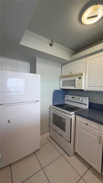 Kitchen featuring white cabinetry, solid-surface countertops, tile flooring, and built-in appliances including a refrigerator, electric range, and over-the-range microwave