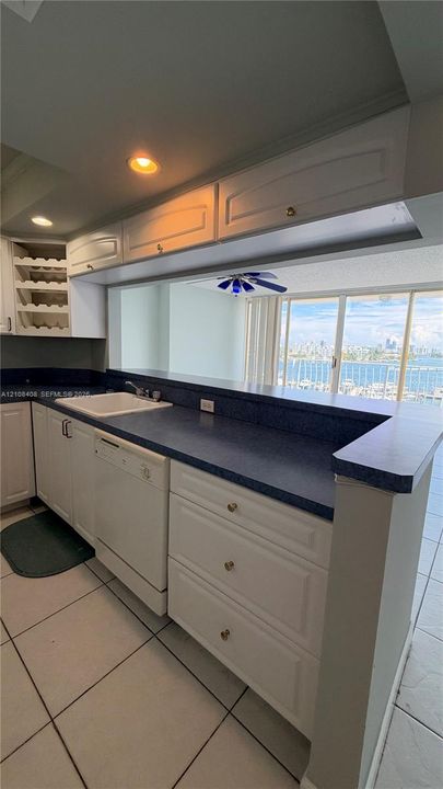 Kitchen featuring white cabinetry with integrated wine storage, contrasting countertops, built-in dishwasher, recessed lighting, and tile flooring