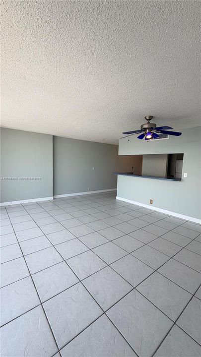 Large-format ceramic tile flooring, neutral wall tones, and a peninsula-style breakfast bar featuring a pass-through counter and a multi-blade ceiling fan with integrated lighting