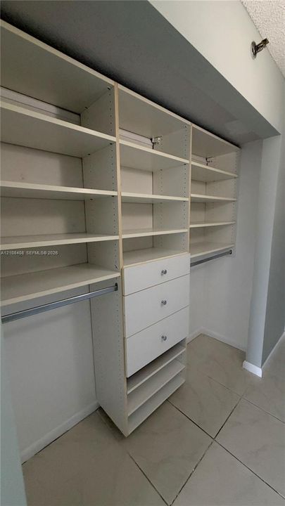 Custom built-in closet organization system featuring adjustable white shelving, integrated drawers with hardware, and metal hanging rods