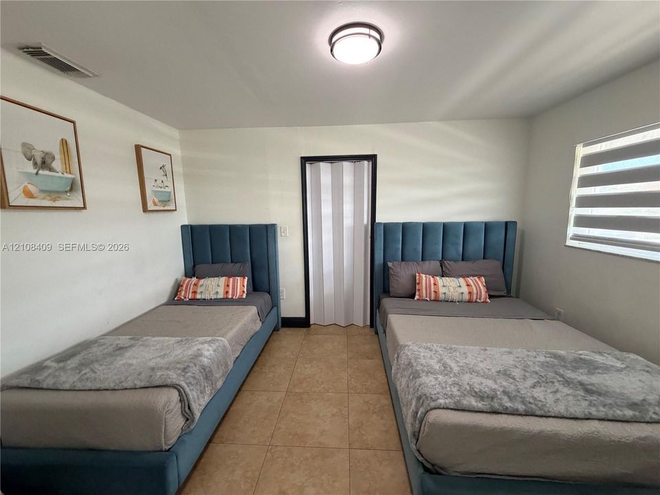 Neutral-toned ceramic tile flooring, neutral wall finish, and white accordion-style closet door with a black frame