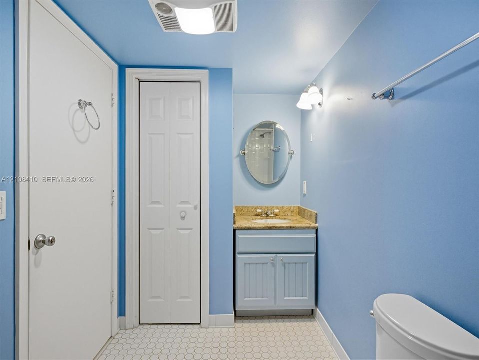 Bathroom featuring a vanity with stone-finish countertop, oval wall mirror, wall-mounted light fixture, bi-fold closet door, and hexagonal tile flooring