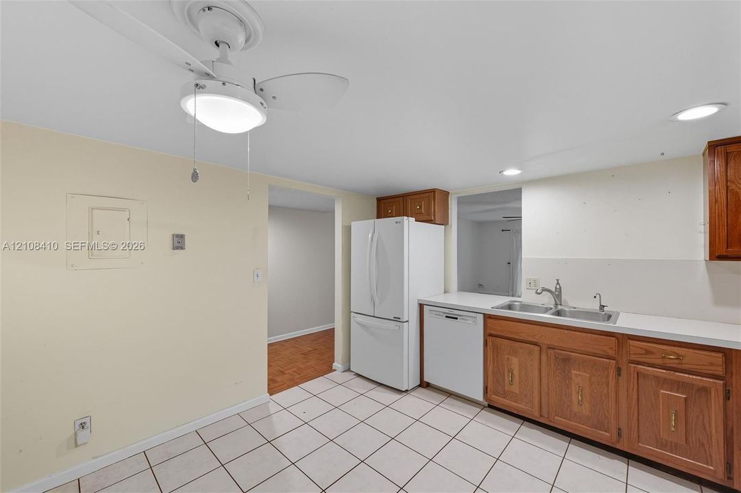 Kitchen featuring wood cabinetry, white appliances, a double-basin stainless steel sink, tiled flooring, and a ceiling-mounted light fixture