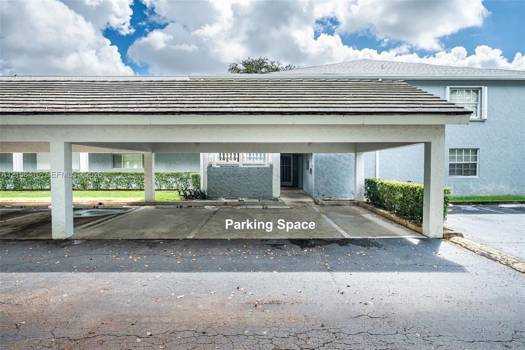 Covered parking structure featuring a shingled roof, concrete flooring, and support pillars, situated at the building exterior