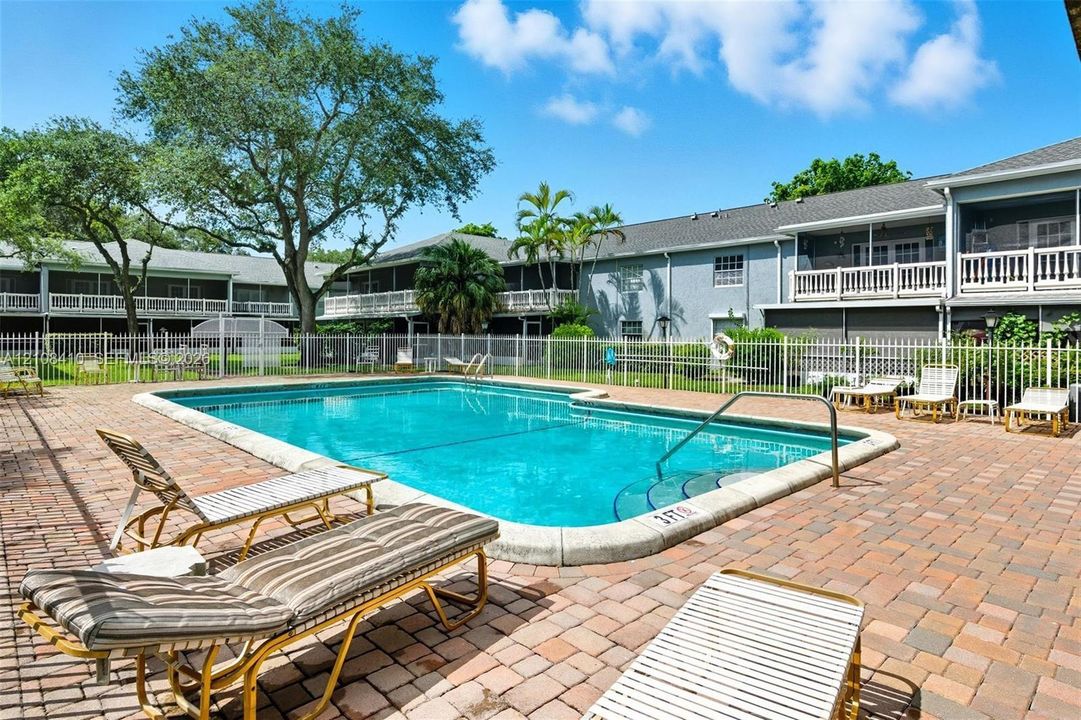 In-ground swimming pool featuring a brick paver surround and perimeter security fencing