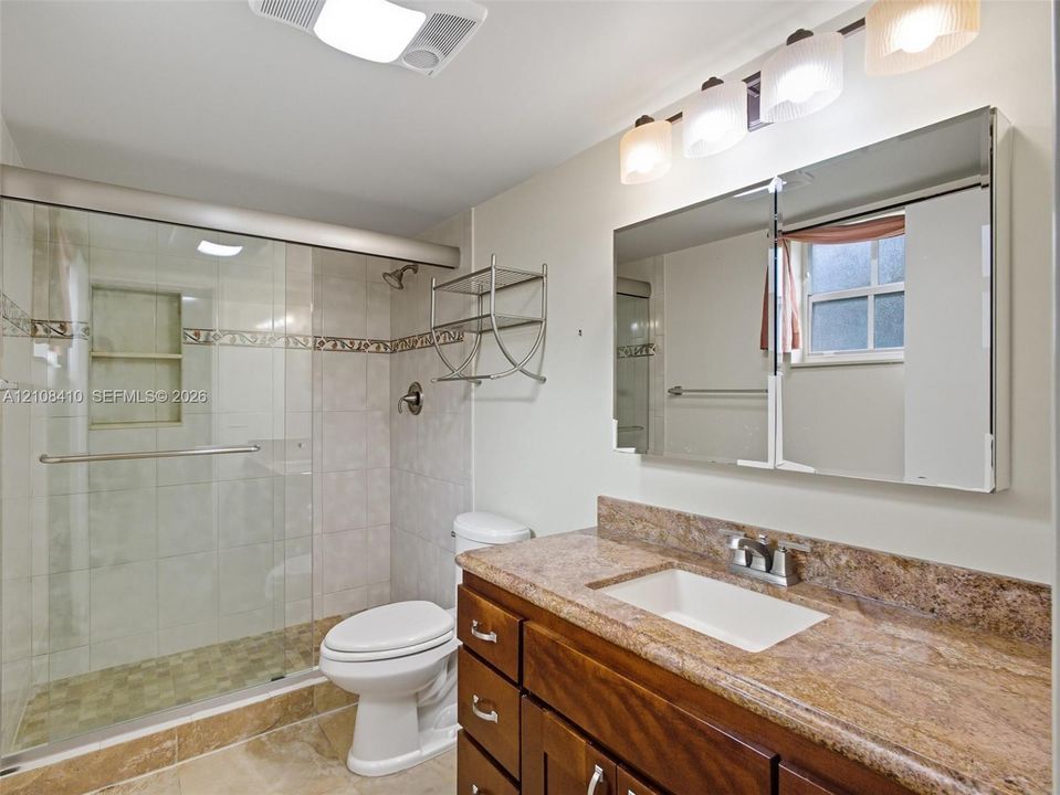 Bathroom featuring a vanity with a stone countertop, an integrated rectangular sink, a glass-enclosed shower with tiled walls and decorative inlay, and a built-in mirrored medicine cabinet