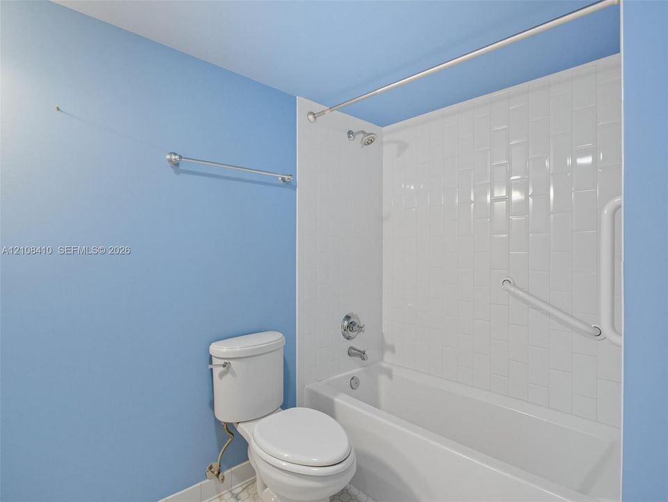 Bathroom featuring a porcelain tub and shower combination with vertical subway tile surround, polished chrome fixtures, and a dual-purpose grab bar