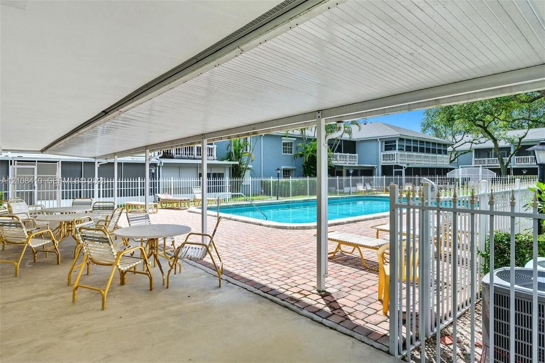 Covered patio with concrete flooring, brick-paver pool deck, in-ground swimming pool, and metal security fencing