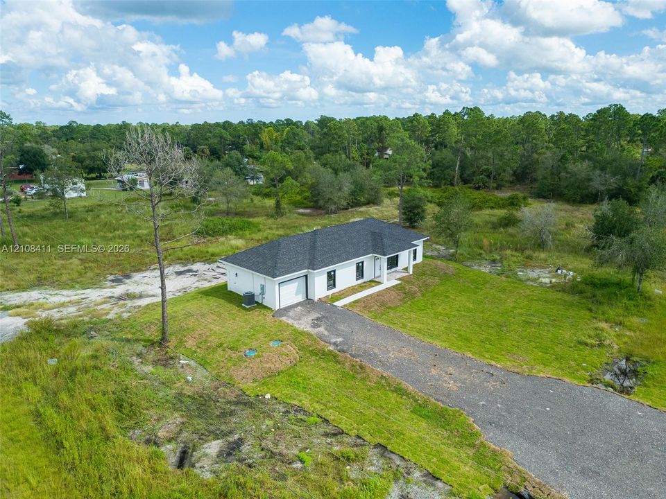 Single-story residence featuring a multi-hip roof, white exterior, attached garage, and a gravel driveway situated on a cleared lot