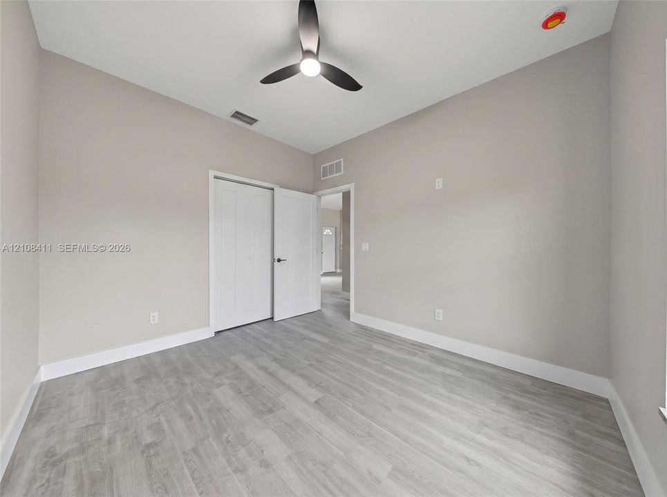 Neutral-toned interior featuring wood-finish flooring, a modern three-blade ceiling fan with integrated lighting, and a dual-panel closet door