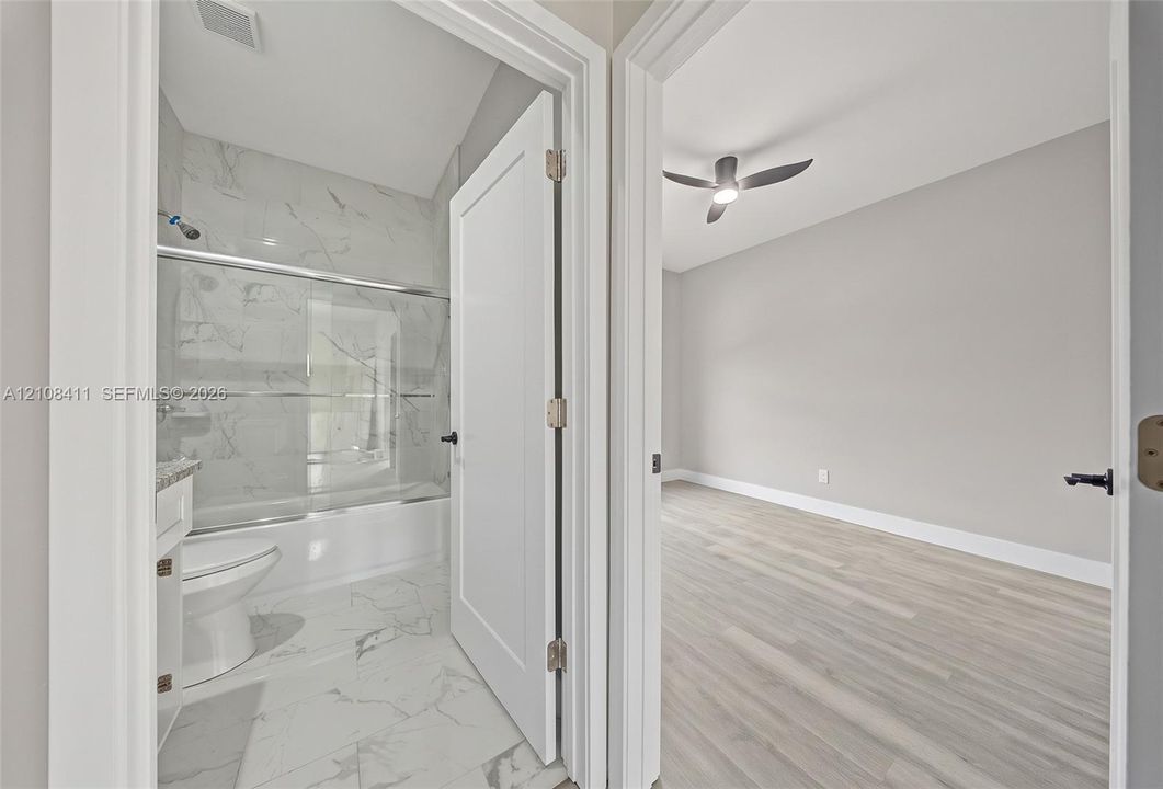 Full bathroom with a tub-shower combination featuring tile surround, and an interior room with wood-finish flooring and a ceiling fan