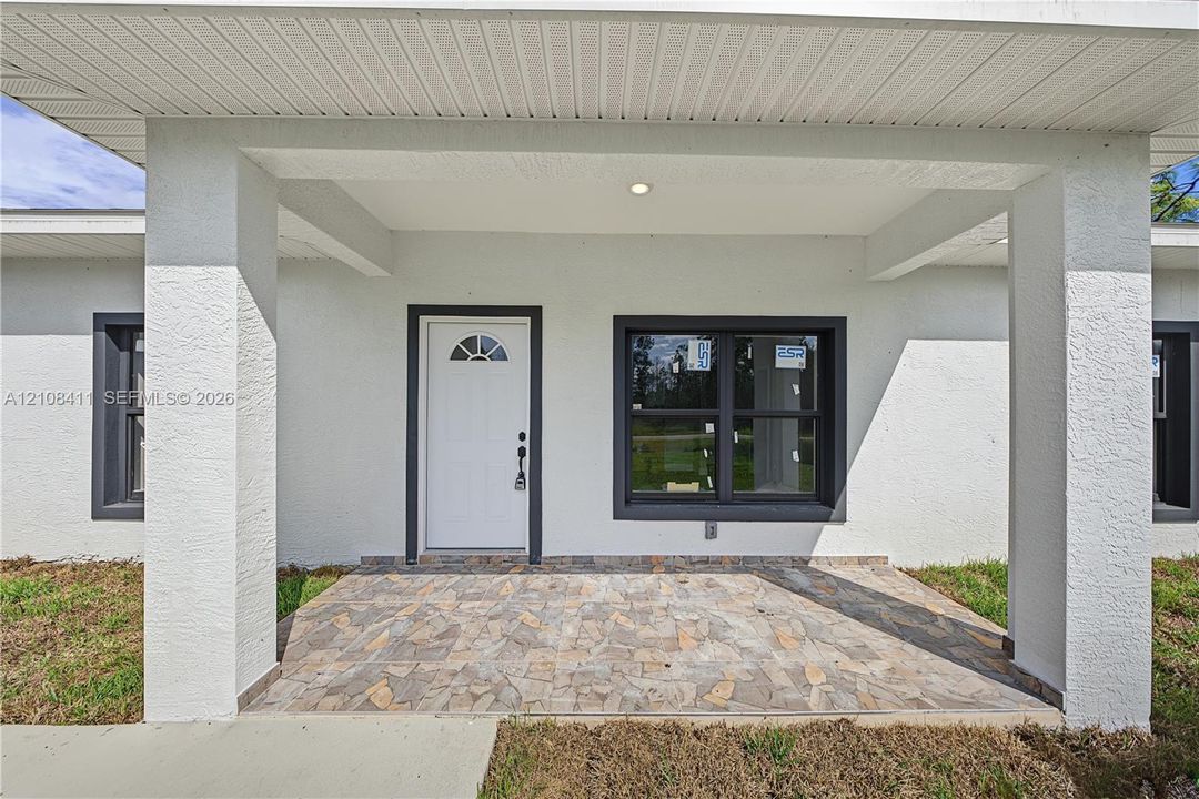 Covered entryway featuring a stone-paver porch, structural support columns, white door with a semi-circular transom window, and dark-framed windows