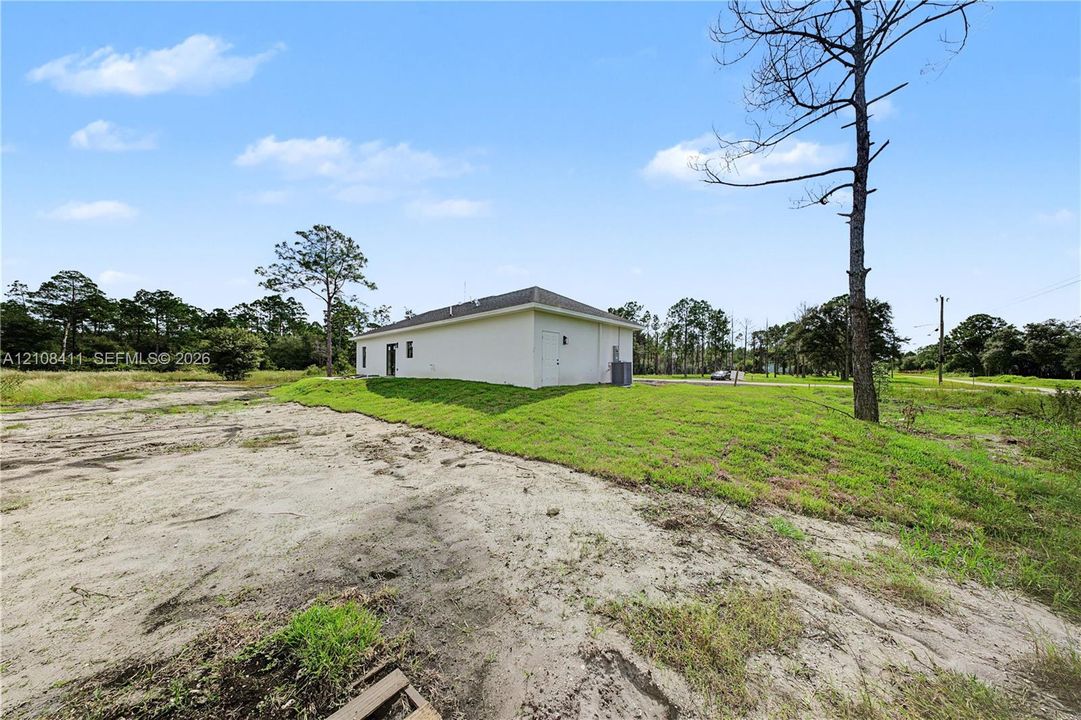 White exterior siding, hipped roofline, and expansive grounds featuring natural vegetation