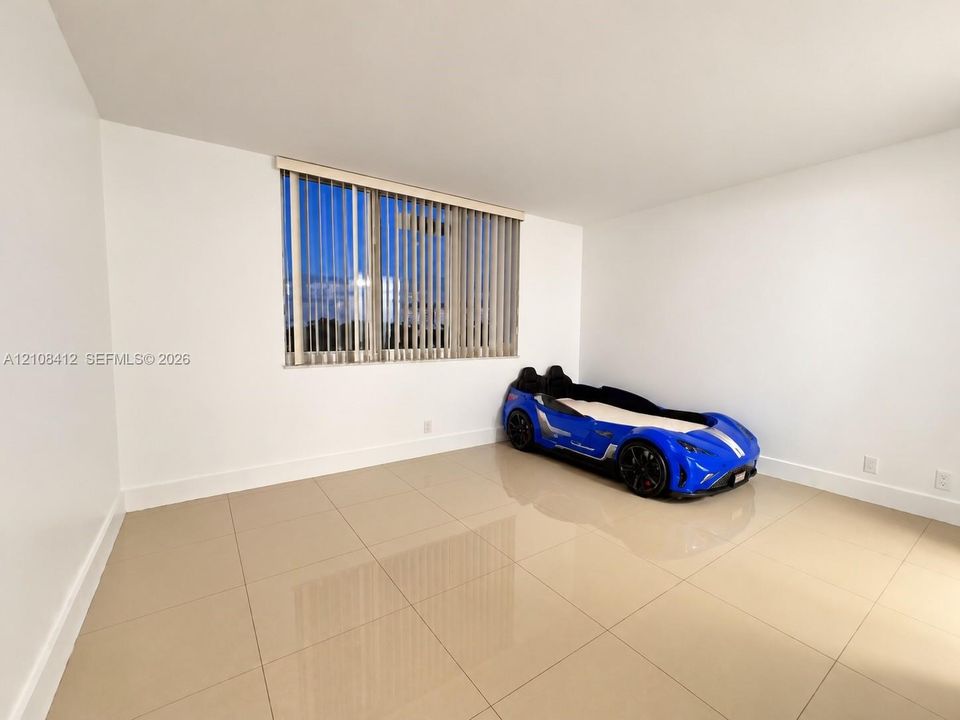 Neutral-toned tile flooring, smooth white wall finishes, and a large window featuring vertical blinds