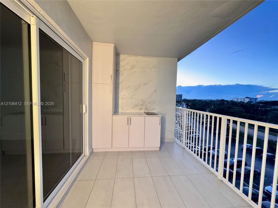 Covered balcony featuring large-format tile flooring, a built-in refreshment station with white cabinetry, a stone-finish backsplash, and a white metal safety railing