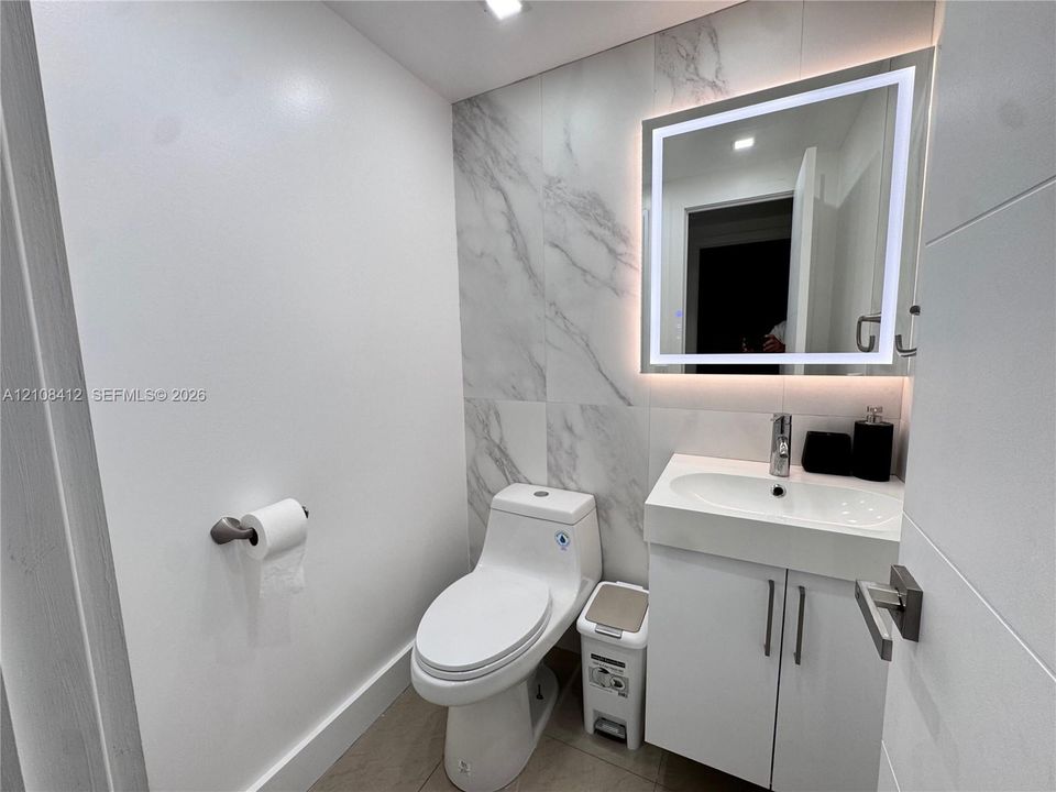 Wall-mounted vanity with integrated sink, large-format stone-patterned tile wall, and LED-backlit mirror