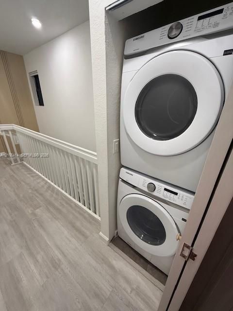 Stacked laundry closet featuring built-in front-load appliances, wood-finish flooring, and white spindle railing