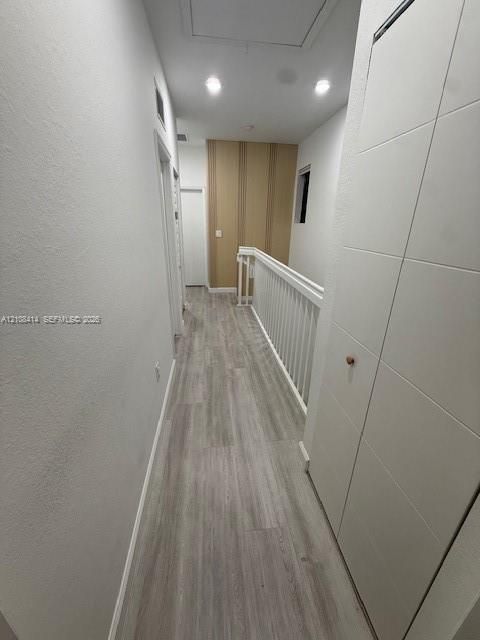 Hallway featuring wood-finish flooring, white paneled doors, recessed ceiling lighting, and a white baluster railing