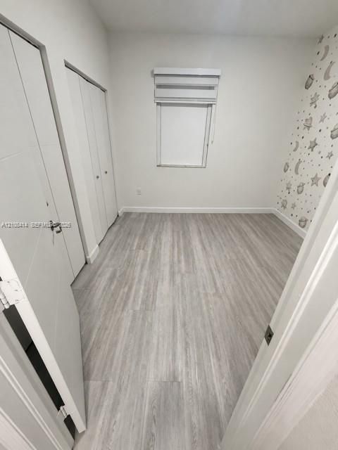 Room featuring wood-finish flooring, dual-panel closet doors, and a window with a mounted roller shade