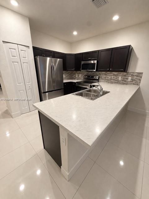 Kitchen featuring a stone-surface island, dark-toned cabinetry, stainless steel appliances, multi-tonal backsplash, and tile flooring