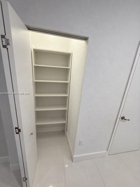 Storage closet featuring built-in shelving and large-format tile flooring
