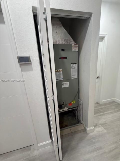 Dedicated mechanical closet featuring a climate control unit with louvered door access and wood-finish flooring
